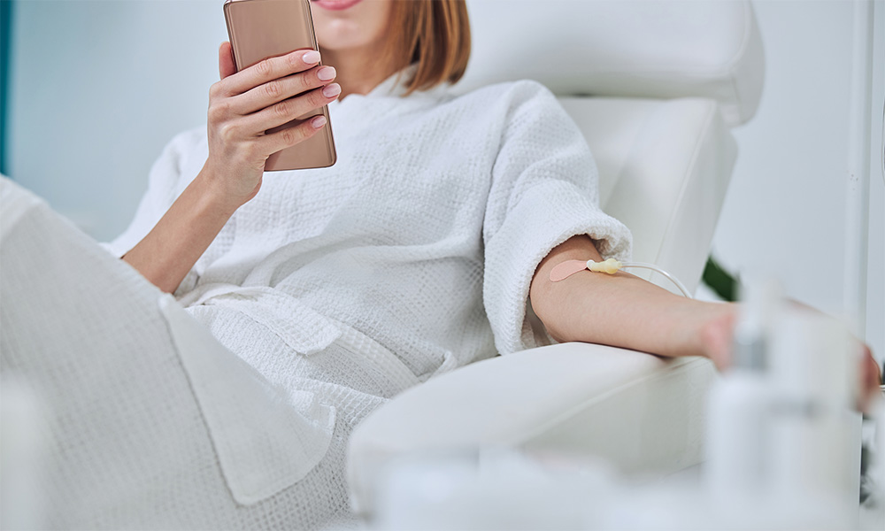 a woman checking her phone while receiving 10X Health IV therapy