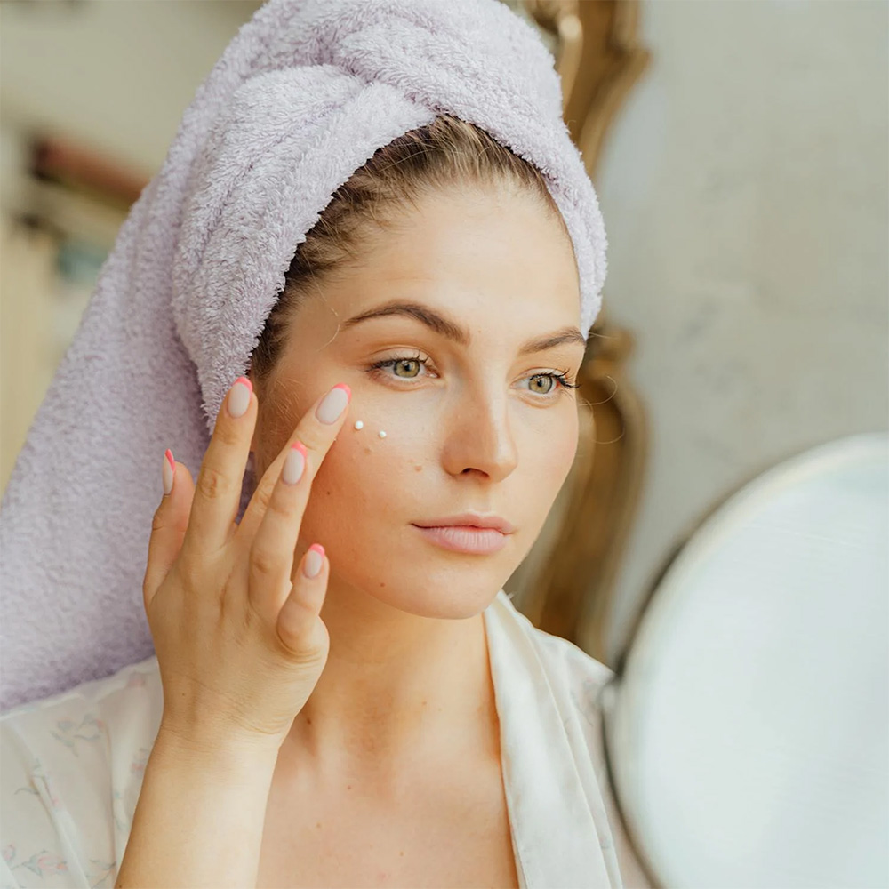 a woman in a bathrobe and hair wrapped in a towel starting to put on makeup