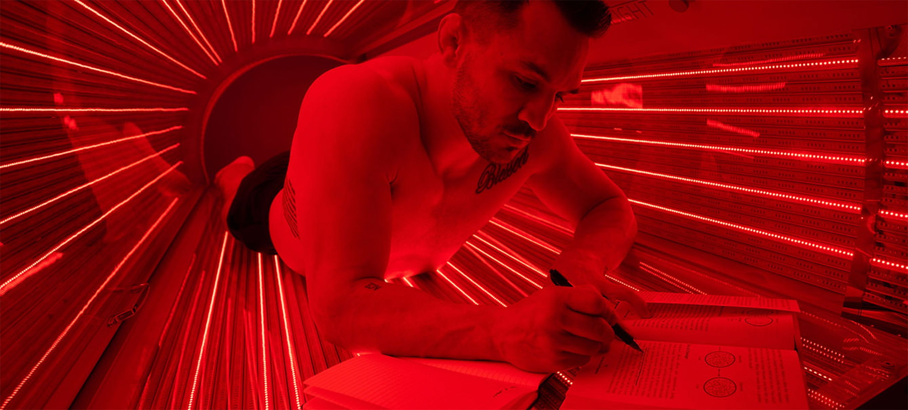 a man taking notes while reading a book inside a red light therapy bed a man taking notes while reading a book inside a red light therapy bed