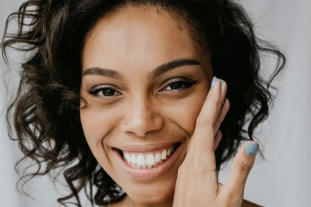a woman smiling while holding her hand to her cheek