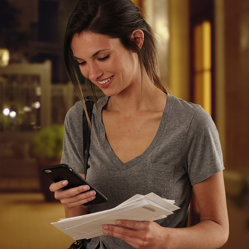 a woman checking her phone while holding mail