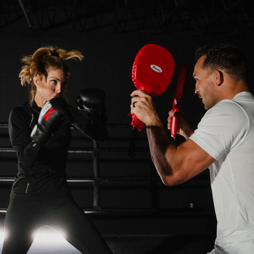 Elena Cardone punches training paddles held by Michael Chandler while wearing 10X boxing gloves