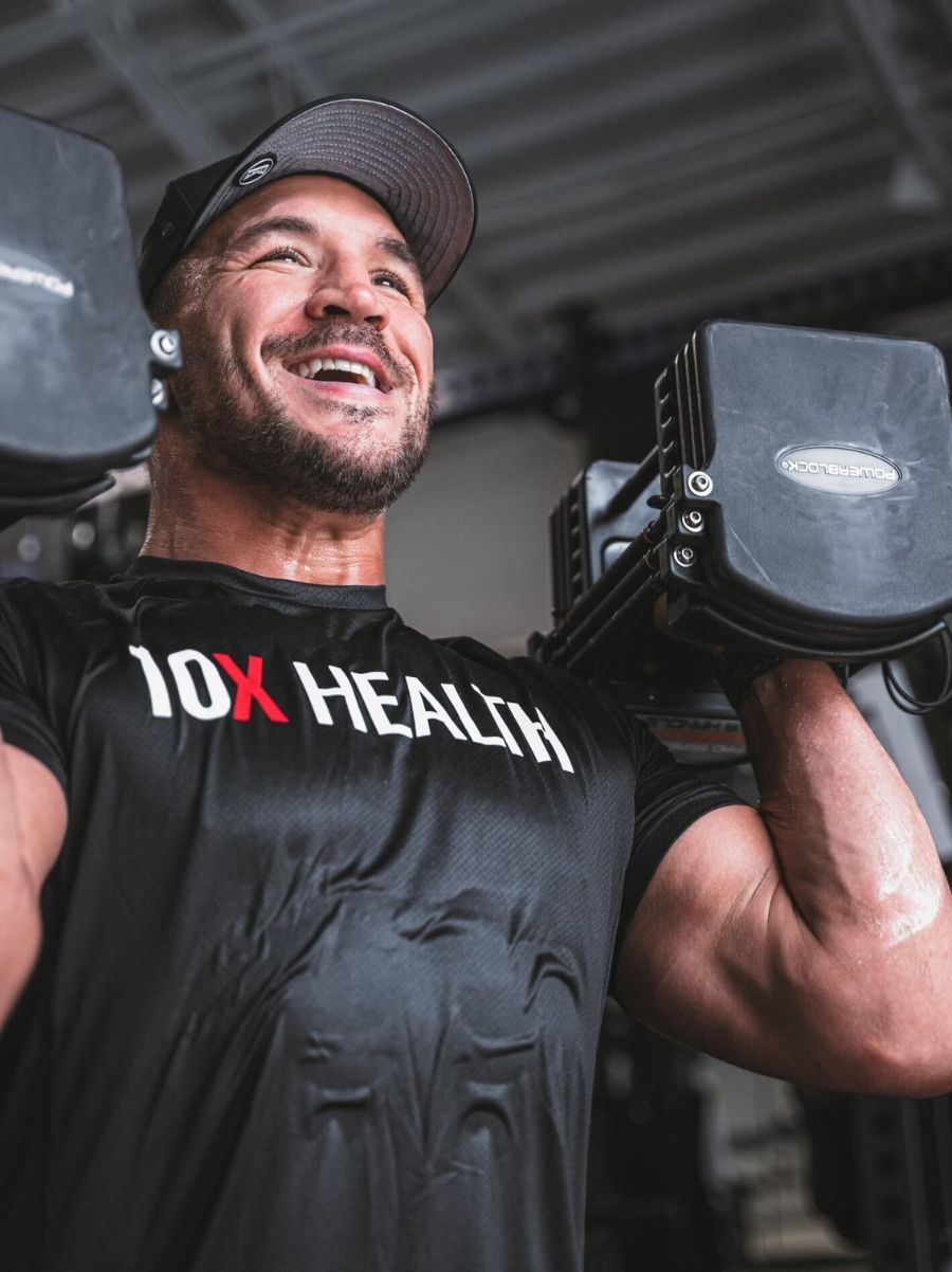 an athlete wearing a 10X Health System shirt smiles while lifting dumbbells an athlete wearing a 10X Health System shirt smiles while lifting dumbbells