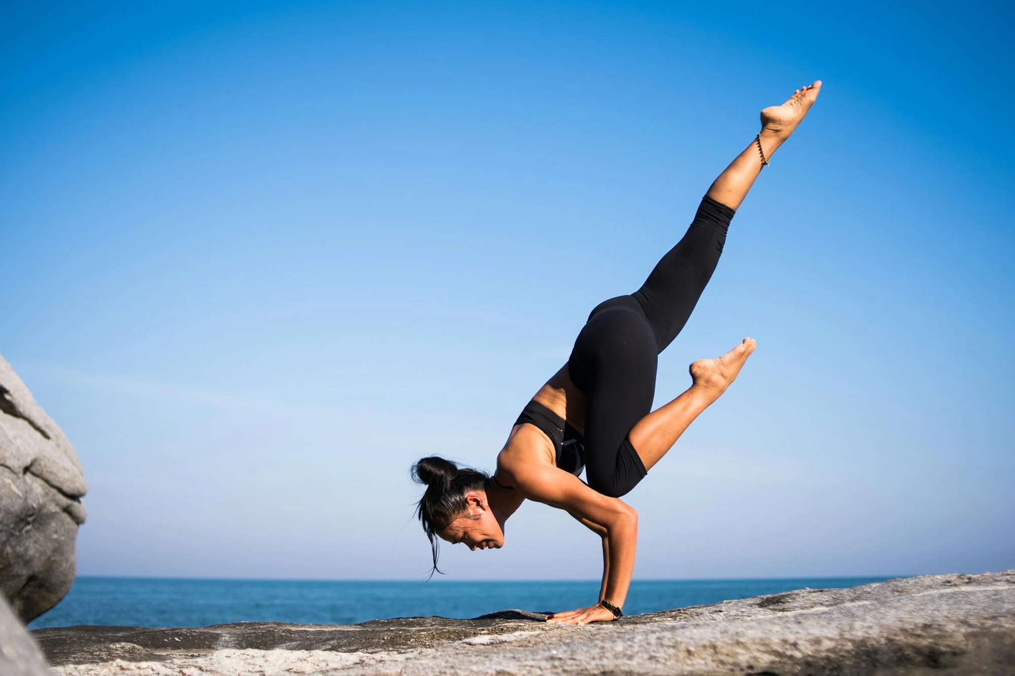 a woman doing a handstand pose on coastal rocks