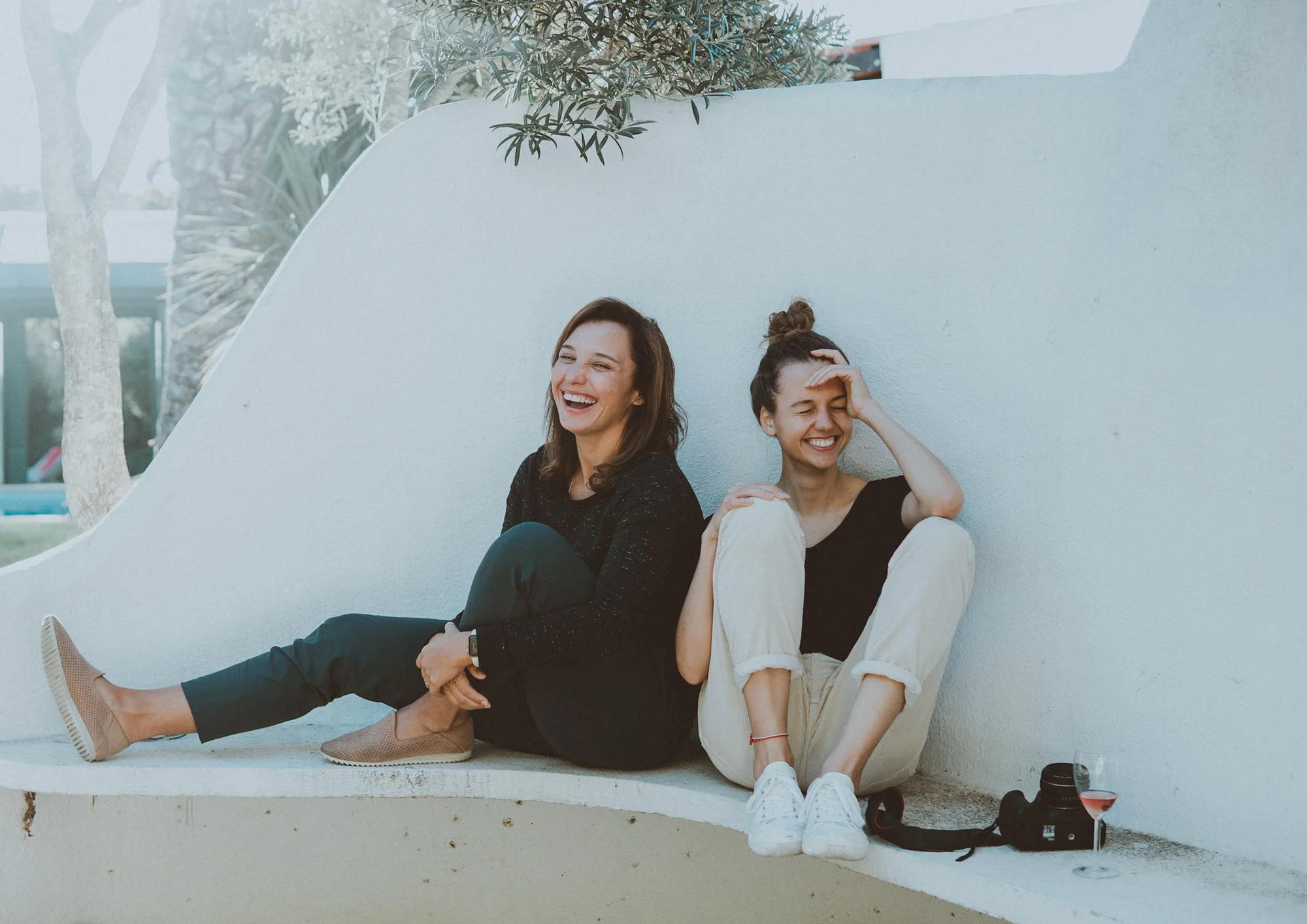 two women laughing while sitting on a bench